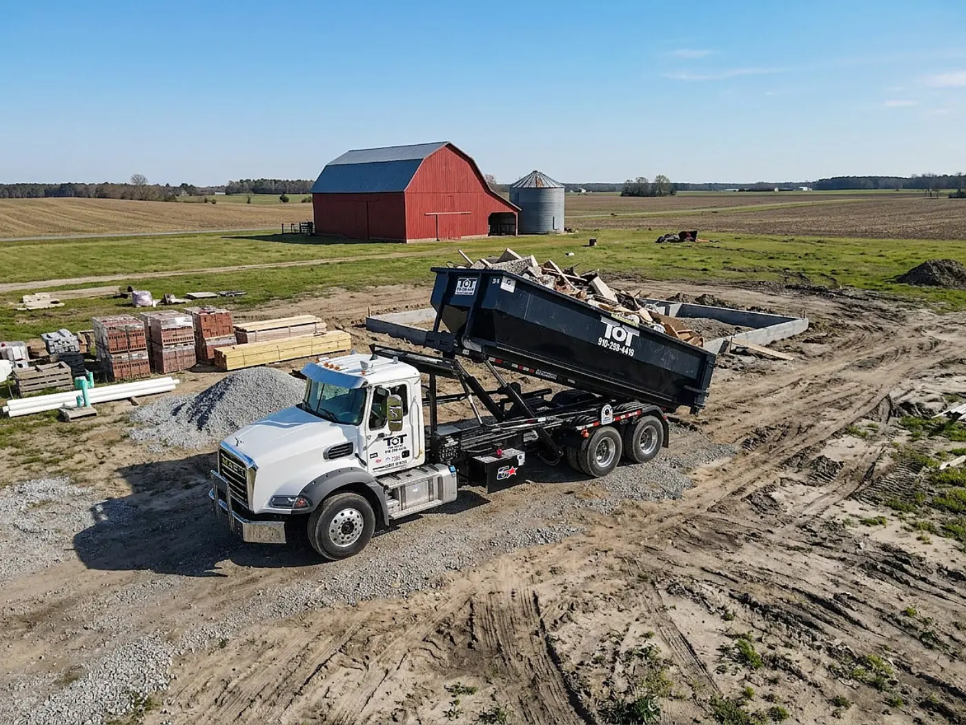 Aerial view of a Tons of Trash roll-off truck lifting a dumpster on a farm